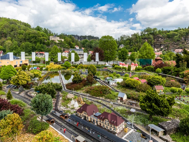 Miniature landscape with model railroad, surrounded by colorful buildings and green trees, under a cloudy sky.
