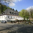 Altenberger Hof Historisches Hotel mit Terrasse unter Bäumen, umrundet von Pflastersteinen und Autos vor blauem Himmel.