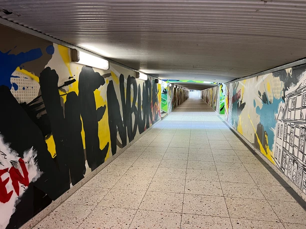 Ein farbenfroher Bahnhofstunnel mit bunten Graffiti-Kunstwerken entlang der Wände und hellem Licht.