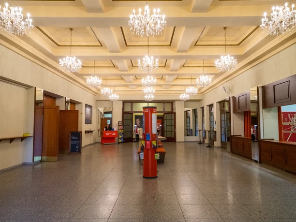 Foyer Musikalische Komödie z podświetlanymi żyrandolami, słupem reklamowym i szatnią