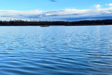 Naturbadesee Pirna-Birkwitz Calm lake with a blue water surface, a small island in the background and a cloudy sky.