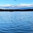 Naturbadesee Pirna-Birkwitz Ruhiger See mit blauer Wasseroberfläche, im Hintergrund eine kleine Insel und bewölkter Himmel.