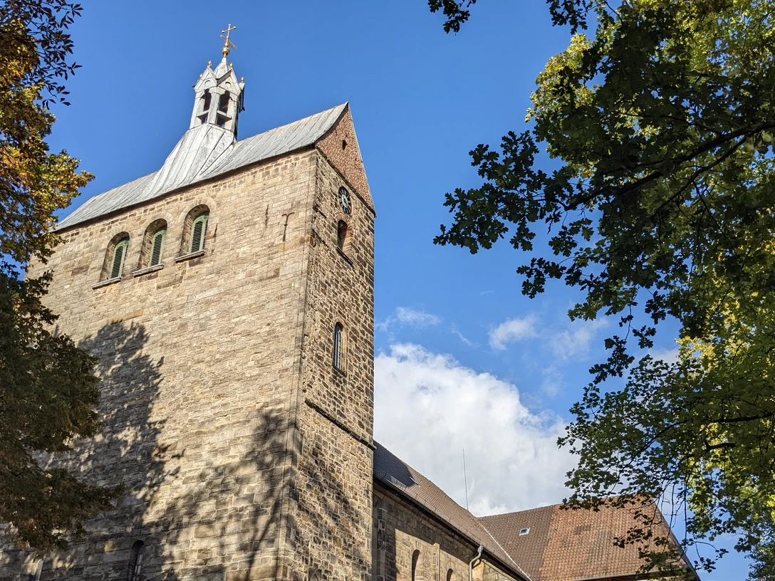 Stiftskirche Stiftskirche mit markantem Turm und gotischen Fenstern, umgeben von grünem Laub unter blauem Himmel.