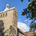 Stiftskirche Stiftskirche mit markantem Turm und gotischen Fenstern, umgeben von grünem Laub unter blauem Himmel.