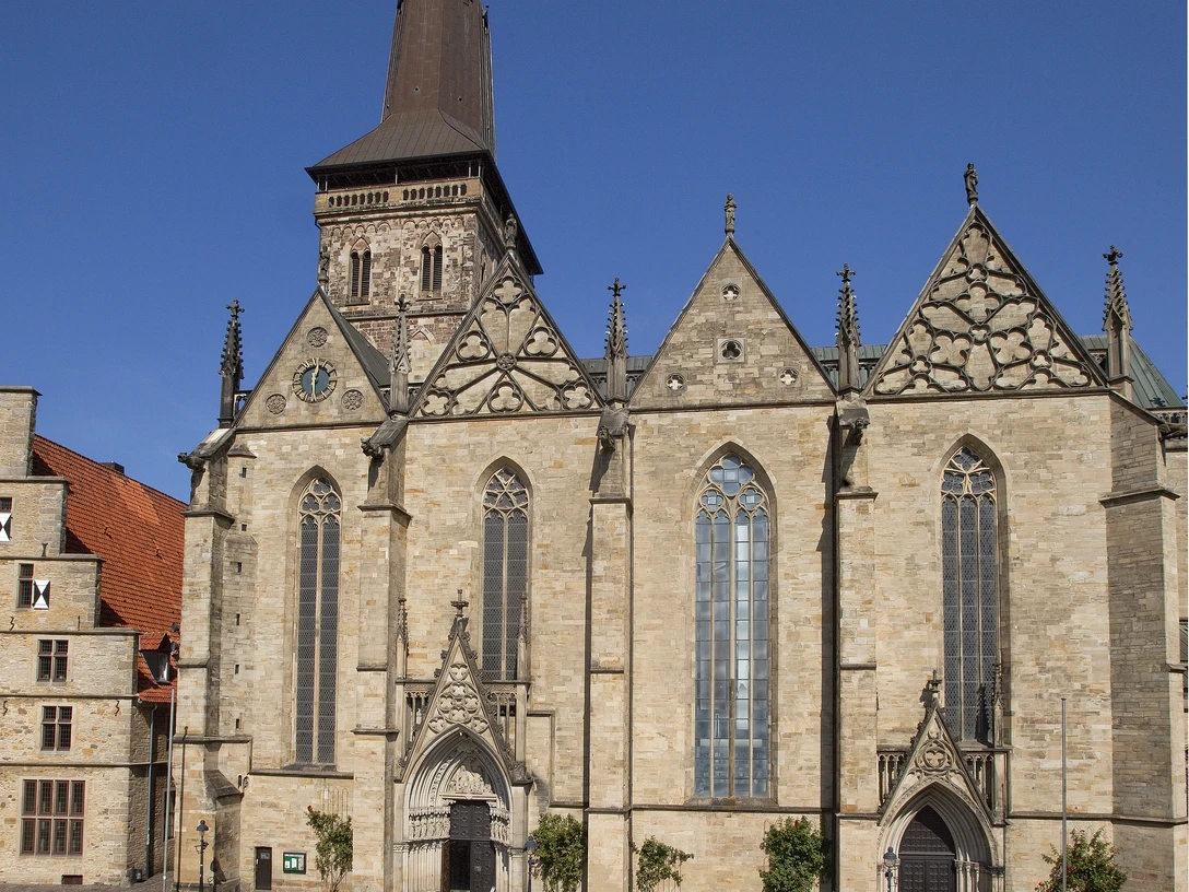 Außenansicht.jpg Eine historische Kirche mit markantem Turm, umgeben von einem gepflasterten Platz unter blauem Himmel.A historic church with a striking tower, surrounded by a paved square under a blue sky.Een historische kerk met een opvallende toren, omgeven door een geplaveid plein onder een blauwe hemel.