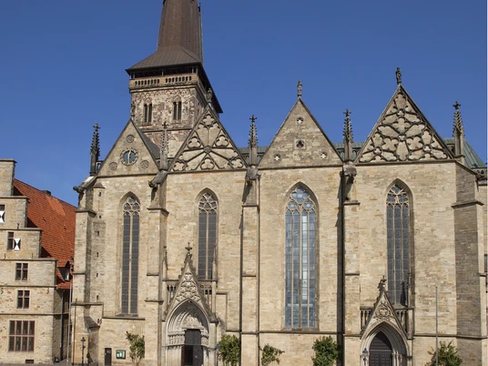 Außenansicht.jpg Eine historische Kirche mit markantem Turm, umgeben von einem gepflasterten Platz unter blauem Himmel.A historic church with a striking tower, surrounded by a paved square under a blue sky.Een historische kerk met een opvallende toren, omgeven door een geplaveid plein onder een blauwe hemel.