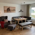 Wohnzimmer der Ferienwohnung Erlenhof Wohnzimmer eingerichtet mit grauem Sessel, grauer Polsterbank und Sitzbank ohne Lehne, moderne Steh-und Hängelampe aus Metall, Holzfußboden.