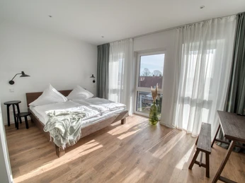 lindaundotto Ein helles, modernes Schlafzimmer mit einem großen Fenster, das viel Tageslicht und eine frische Atmosphäre einlässt.