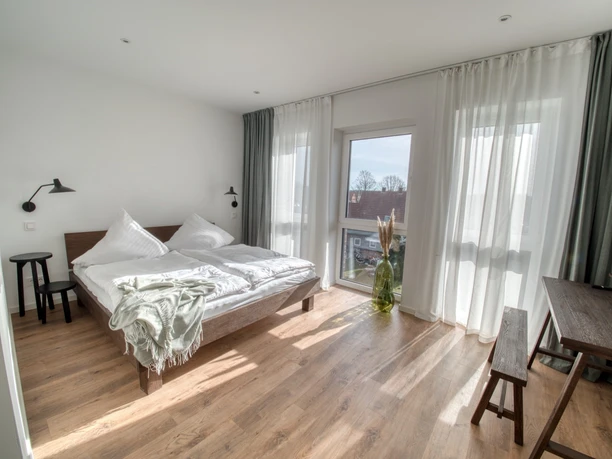 lindaundotto Ein helles, modernes Schlafzimmer mit einem großen Fenster, das viel Tageslicht und eine frische Atmosphäre einlässt.