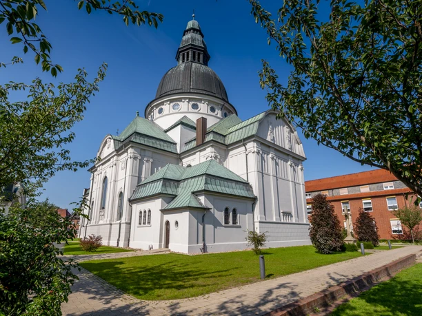 2020_09_15_NZ6_0387.jpg Weiße Kirche mit großer Kuppel und grünen Dächern, umgeben von Rasen und Bäumen bei Sonnenschein.