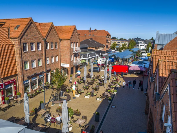 2020_09_18_DJI_0499.jpg Belebte Einkaufsstraße in Haren mit roten Backsteinhäusern, Straßencafés und bunten Marktständen.