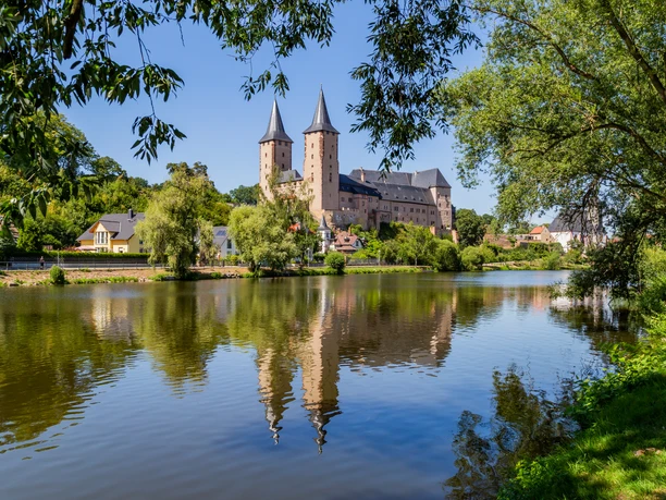 Widok ogólny zamku Rochlitz z rzeką Mulde na pierwszym planie, otoczony zielenią drzew, ścieżka rowerowa Mulde, szlak Luther Trail Saxony