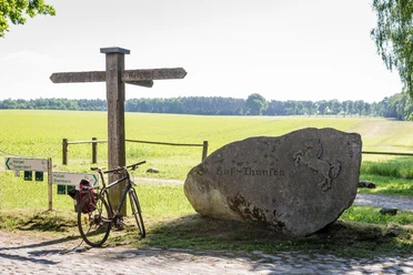 Thansen Fahrrad und Wegweiser am Stein mit Pferderelief vor weiten Feldern in Thansen.