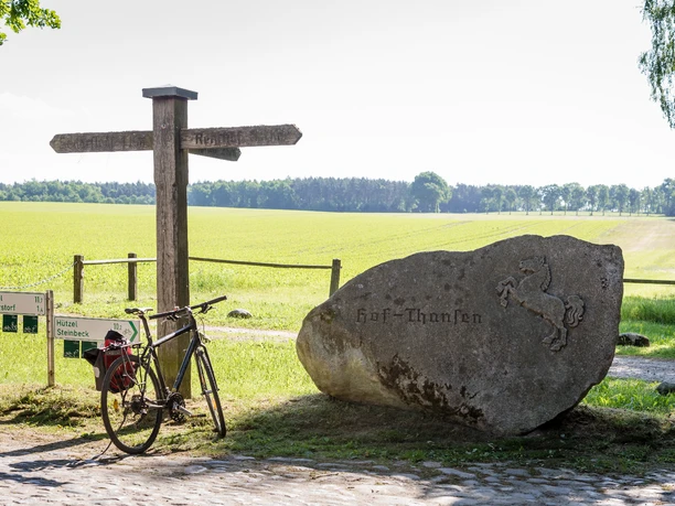 Thansen Fahrrad und Wegweiser am Stein mit Pferderelief vor weiten Feldern in Thansen.