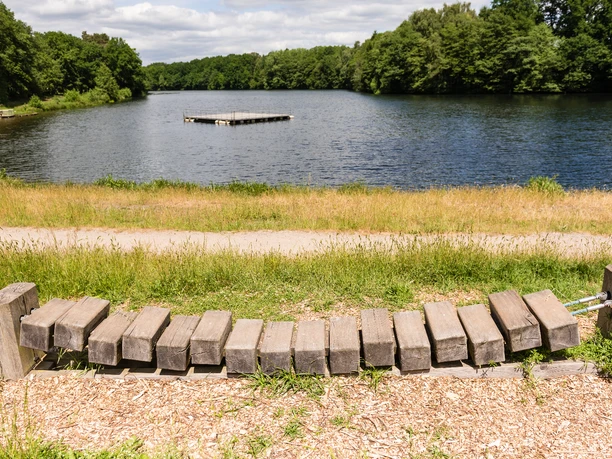 Blick auf den Lopausee mit Fitnessgerät aus Holz im Vordergrund und Wald im Hintergrund.