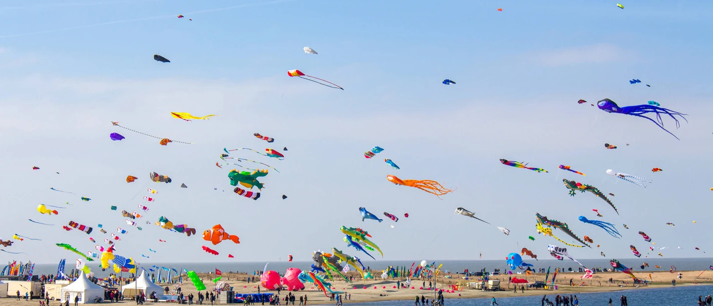 Buesum-Drachenflugtage-Familienlagune02.jpg Bunte Drachen am Himmel über einer Lagune. Im Hintergrund ist das Meer.