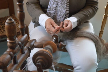 Spinnen Eine Person spinnt Wolle auf einem traditionellen Spinnrad, Hände konzentriert fadenführend.