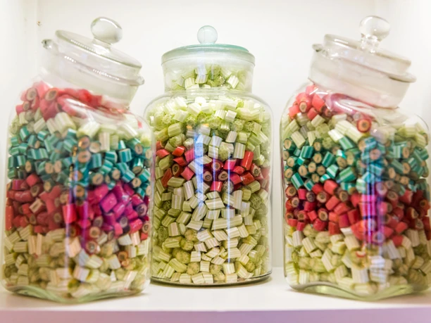 Three glass containers with colorful sweets in red, green and blue on a shelf; the atmosphere is nostalgic and inviting.
