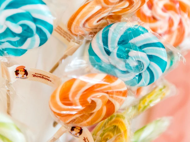 Colorful lollipops in blue-white and orange-white, wrapped in cellophane, with label "handmade sweets" on a wooden stick.
