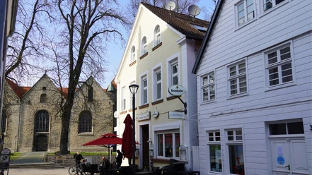 Zwei historische Gebäude in Brakel, eines mit Satteldach, davor ein Café mit roten Schirmen.