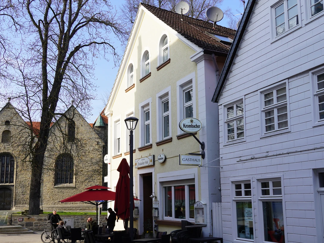 Zwei historische Gebäude in Brakel, eines mit Satteldach, davor ein Café mit roten Schirmen.