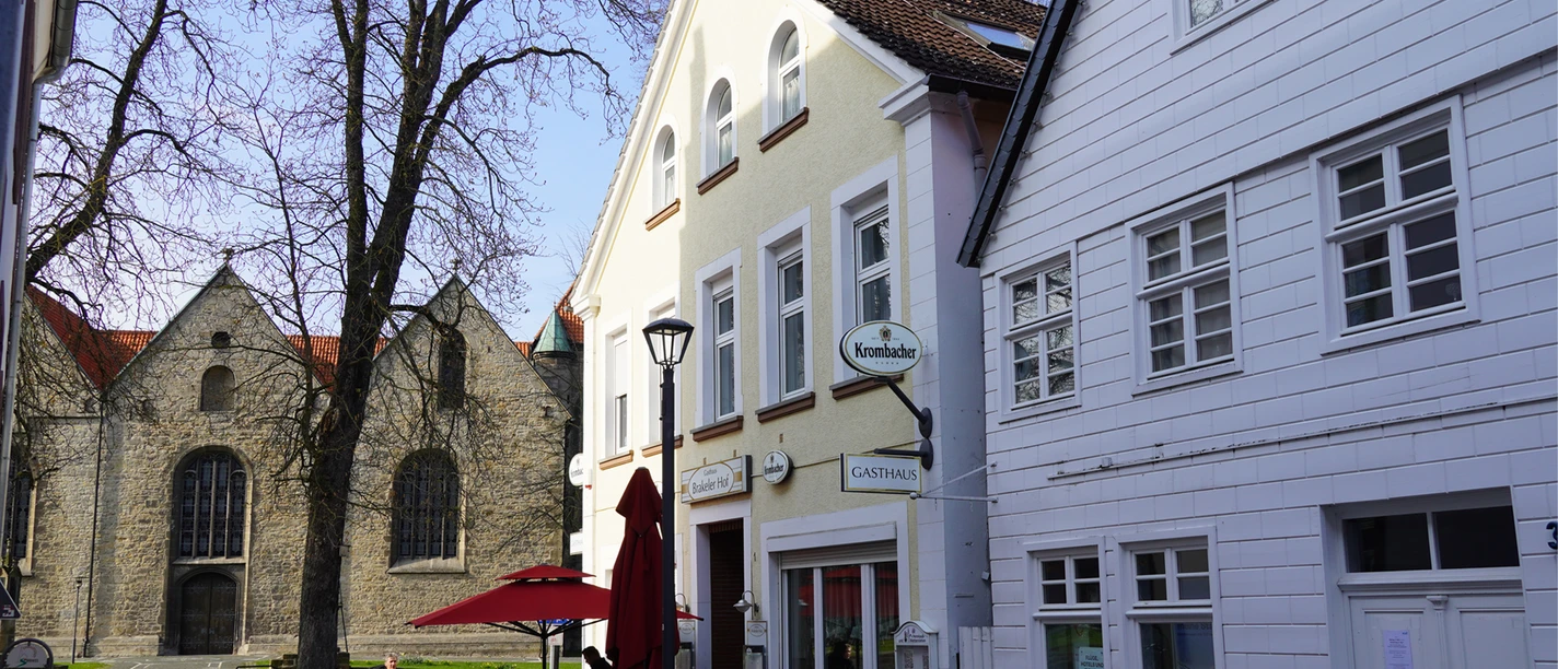 Zwei historische Gebäude in Brakel, eines mit Satteldach, davor ein Café mit roten Schirmen.