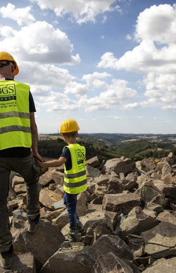 Steinbruch Ein Erwachsener und ein Kind in Schutzhelmen und Westen stehen auf einem Steinbruch, blicken in die Ferne.