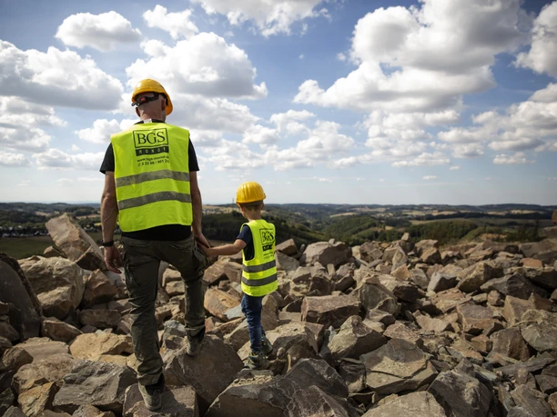 Steinbruch Ein Erwachsener und ein Kind in Schutzhelmen und Westen stehen auf einem Steinbruch, blicken in die Ferne.