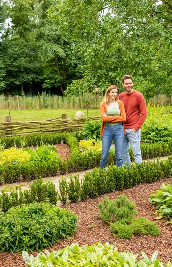 Ein lächelndes Paar spaziert durch einen gepflegten, grünen Garten mit umgebenden Bäumen.