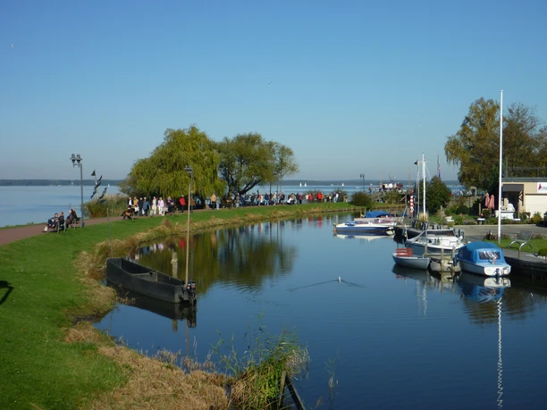 Boote im Hafen von Steinhude, mit ruhigem Wasser und Menschen, die die Promenade entlangspazieren.