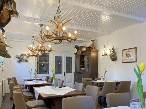 Útulná restaurace s dřevěným nábytkem, lustry z paroží a taxidermiemi na stěnách; žluté tulipány na stolech dodávají restauraci barevný nádech.