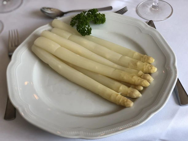 White asparagus spears lie on a white plate, decorated with a sprig of parsley.