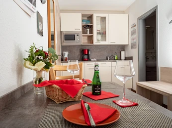 Apartment Alme_Essbereich.jpg Essbereich in einer modernen Küche, gedeckter Tisch mit Blumen und Getränken vor eleganter Einrichtung.