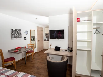 Apartment Alme_Raum.jpg Modern eingerichtetes Apartment mit Holzboden, Esstisch, Küchenzeile, Kleiderschrank und TV.