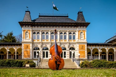 CSMotiv2022©JanBräuer.jpg Großes Kontrabass vor historischer Villa mit verzierten Fassaden und Türmen bei sonnigem Wetter.