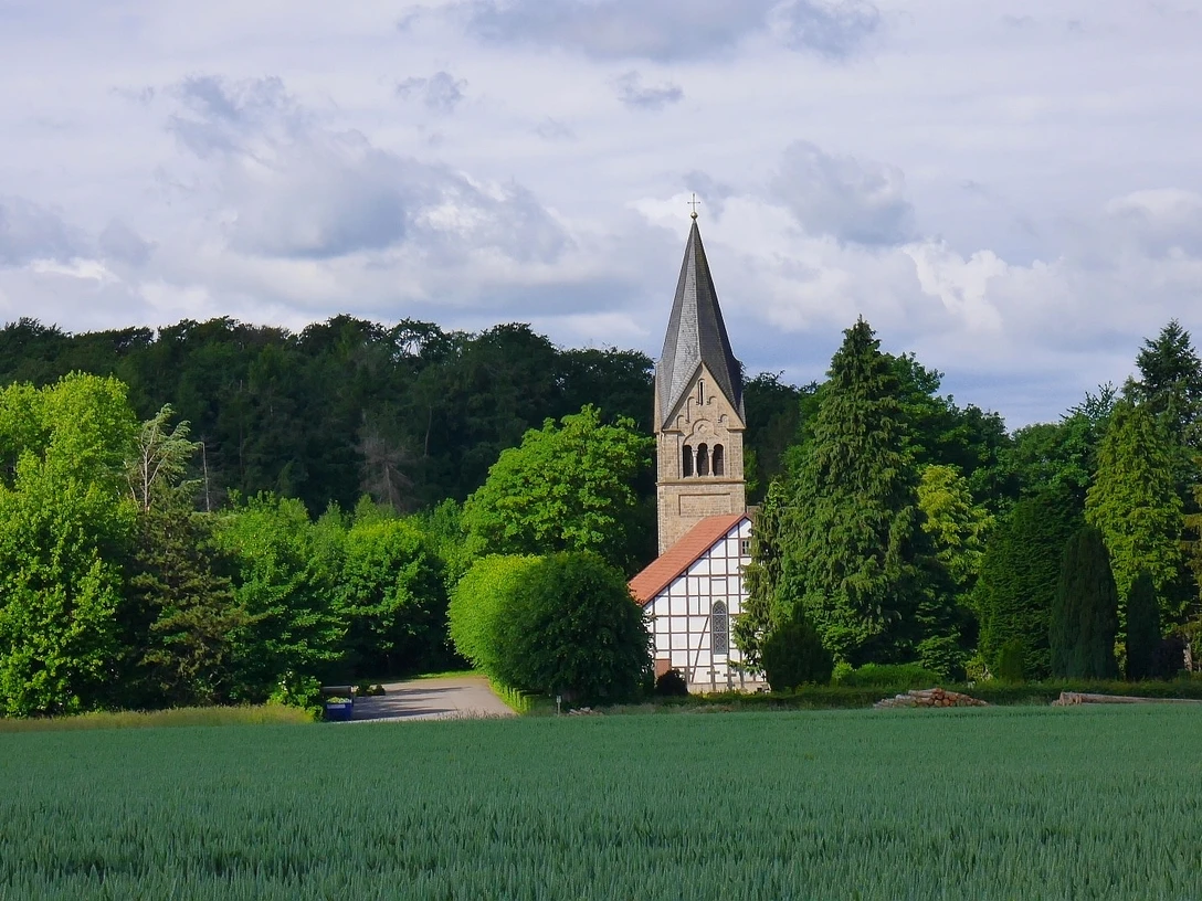 Fachwerkkirche in Bergkirchen nahe Hollenstein Eine Fachwerkkirche steht malerisch vor einem Wald. Im Vordergrund dehnt sich ein Feld aus.