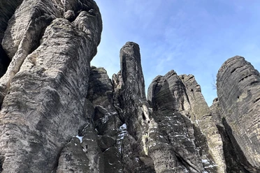 High, gray rock formations with scattered patches of snow rise up under a clear blue sky.