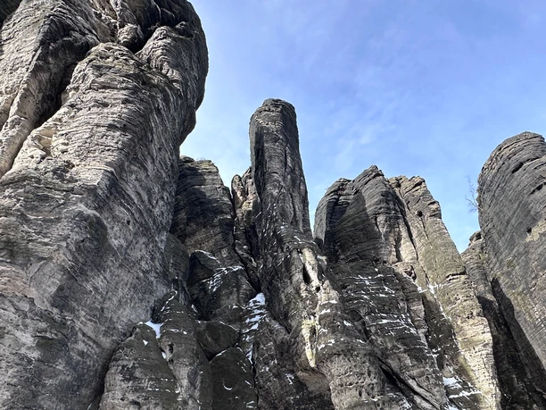High, gray rock formations with scattered patches of snow rise up under a clear blue sky.