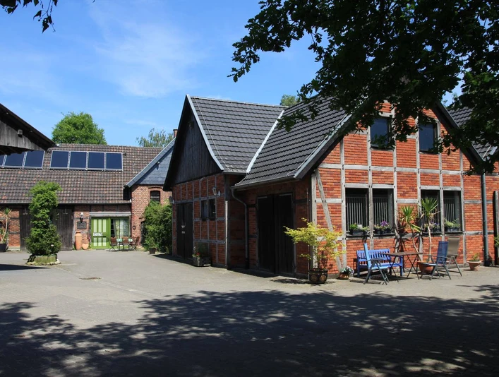 Ferienwohnung-Bergmann-Scholvien.jpg Ferienwohnung in einem historischen Fachwerkhaus mit Innenhof, umgeben von Bäumen und Gartenmöbeln.