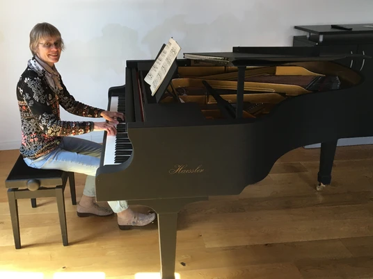 Annette Liss am Haessler-Flügel Die Pianistin Annette Liss sitzt am Klavier und lächelt in die Kamera.