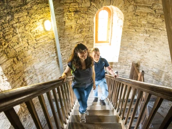 Bielefeld-Sparrenburg-Teutoburger-Wald-Tourismus-D-Ketz-019-2.jpg Zwei fröhliche Personen steigen eine steinerne Turmtreppe hinauf, erhellt von natürlichem Licht.