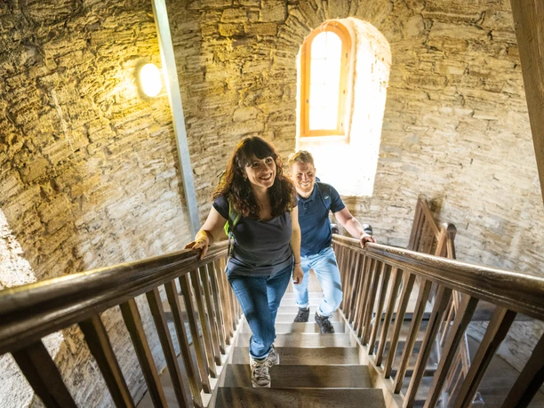 Bielefeld-Sparrenburg-Teutoburger-Wald-Tourismus-D-Ketz-019-2.jpg Zwei fröhliche Personen steigen eine steinerne Turmtreppe hinauf, erhellt von natürlichem Licht.