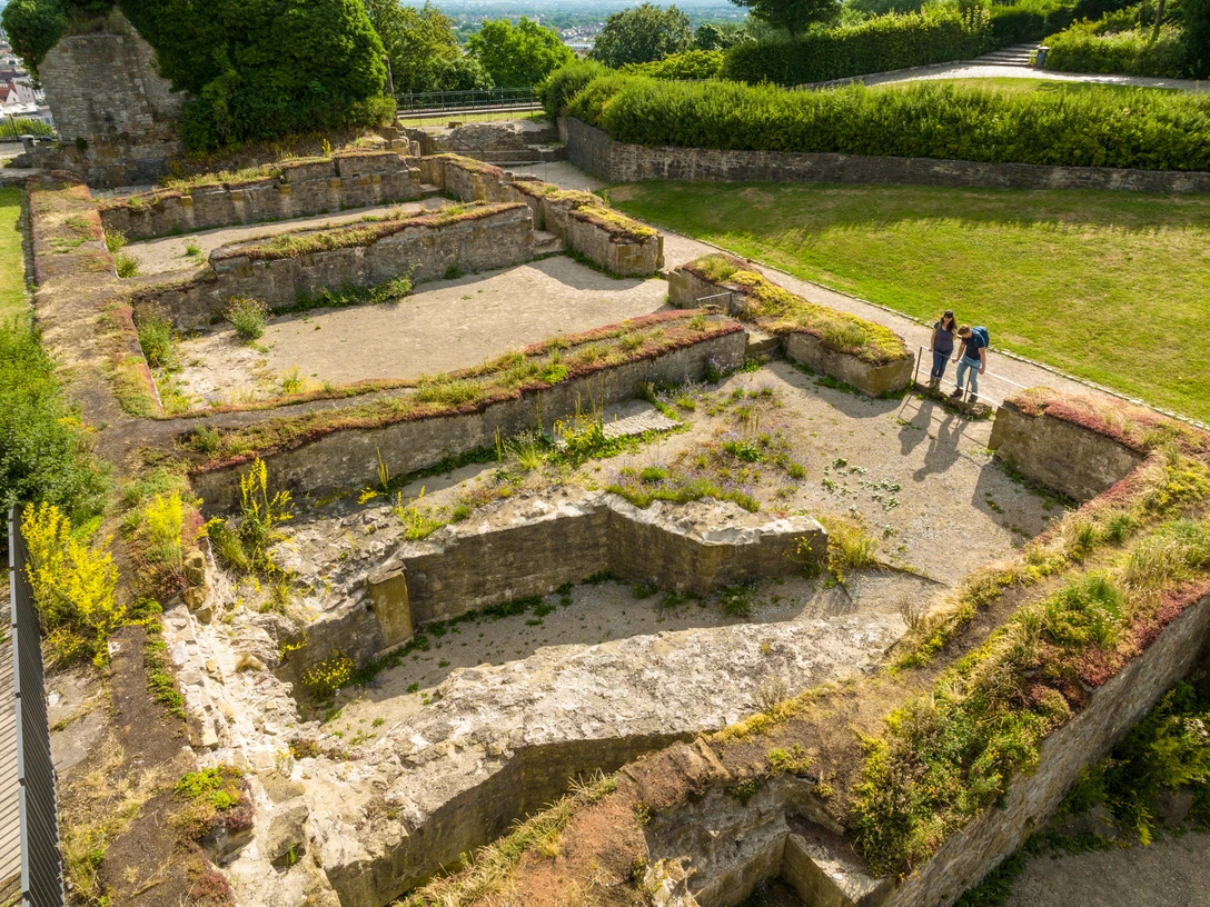 Bielefeld-Sparrenburg-Teutoburger-Wald-Tourismus-D-Ketz-030-2.jpg Ruinen eines antiken Gebäudes, umgeben von grüner Landschaft; drei Menschen betrachten die Überreste.