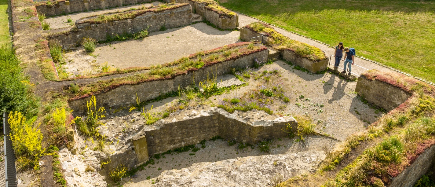 Bielefeld-Sparrenburg-Teutoburger-Wald-Tourismus-D-Ketz-030-2.jpg Ruinen eines antiken Gebäudes, umgeben von grüner Landschaft; drei Menschen betrachten die Überreste.