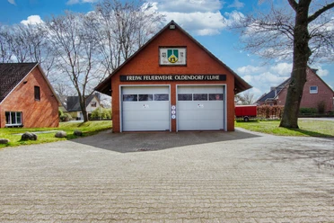 feuerwehrhaus-oldendorfluhe-2023.jpg Backsteinbau der Freiwilligen Feuerwehr Oldendorf mit zwei grauen Toren und Wappen an der Giebelseite