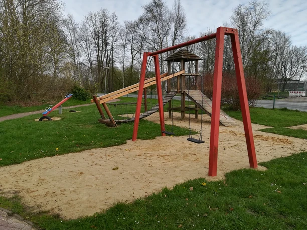 Spielplatz Oberndorf Bentwisch Rote Schaukel, Wippe und Holzkletterturm laden Kinder auf dem grünen Spielplatz zum Spielen ein.