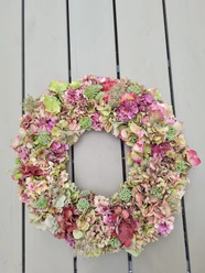 Hortensienkranz.jpg Ein Kranz aus getrockneten Hortensienblüten in Rosa- und Grüntönen liegt auf einem Holztisch.