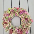 Hortensienkranz.jpg Ein Kranz aus getrockneten Hortensienblüten in Rosa- und Grüntönen liegt auf einem Holztisch.