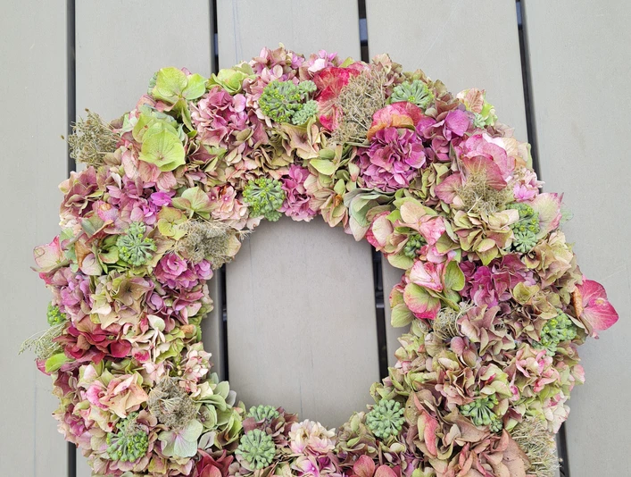 Hortensienkranz.jpg Ein Kranz aus getrockneten Hortensienblüten in Rosa- und Grüntönen liegt auf einem Holztisch.