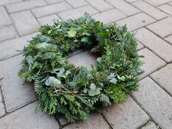 Adventskranz Ein Adventskranz aus frischem Tannengrün mit Eukalyptuszweigen liegt auf grauen Pflastersteinen.